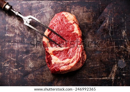 Raw fresh meat Ribeye Steak and meat fork on dark metal backgrou