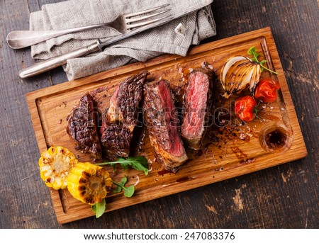 Sliced medium rare grilled Beef steak Ribeye with corn and cherry tomatoes on cutting board on wooden background