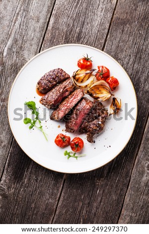 Sliced medium rare grilled Beef steak Ribeye with grilled onions and cherry tomatoes on plate on wooden background