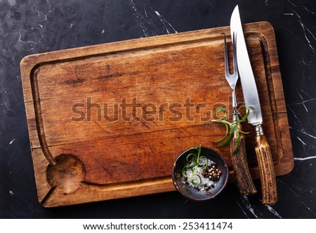 Chopping cutting board, seasonings and rosemary with fork and knife carving set on dark marble background