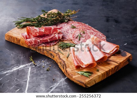 Cold meat plate with prosciutto and salami on olive wood board on dark marble background