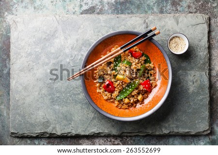 Fried Rice with vegetables in red bowl and green tea on stone slate background
