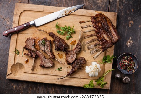 Roasted lamb ribs and kitchen knife on wooden cutting board on dark background