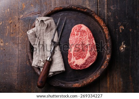 Raw fresh marbled meat Black Angus Steak Ribeye and meat fork on dark background