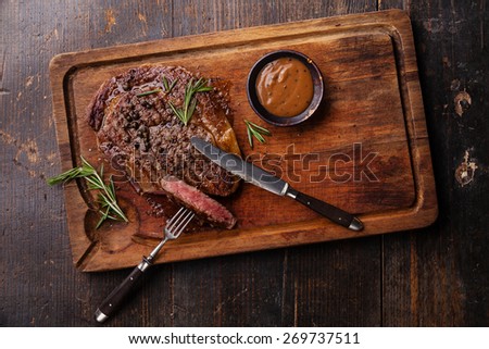 Grilled Black Angus Steak Ribeye and Pepper sauce on meat cutting board on dark wooden background