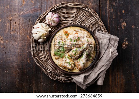 Roasted chicken with creamy garlic sauce in clay pan ketsi on dark wooden background