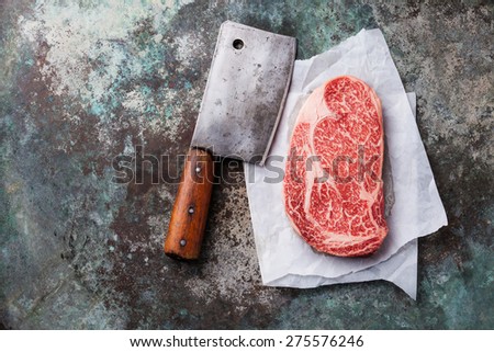 Raw fresh marbled meat Black Angus Steak Ribeye and meat cleaver on metal background