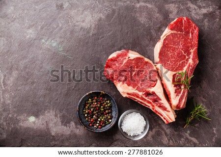 Heart shape Raw fresh meat Ribeye Steak with rosemary, pepper and salt on stone slate background
