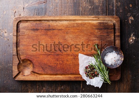 Chopping board, seasonings and rosemary on dark wooden background