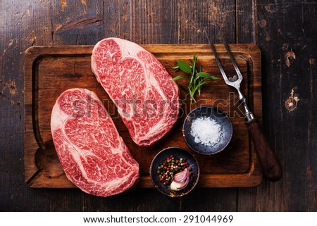Two Raw fresh marbled meat Black Angus Steak Ribeye, seasonings and meat fork on dark wooden background