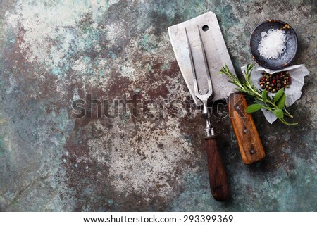 Vintage meat Fork and Cleaver with seasonings on metal background