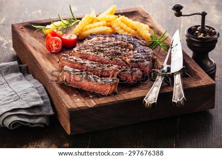 Sliced medium rare grilled Steak Ribeye Black Angus with french fries on serving board block on wooden background
