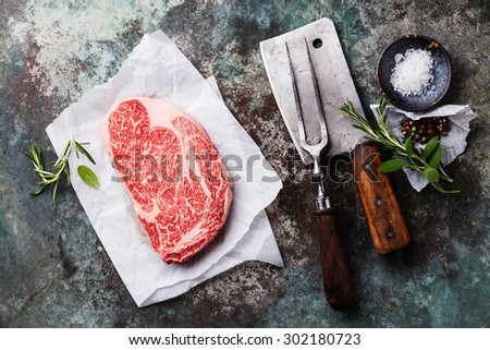 Raw fresh marbled meat Black Angus Steak, seasonings, meat fork and cleaver on metal background
