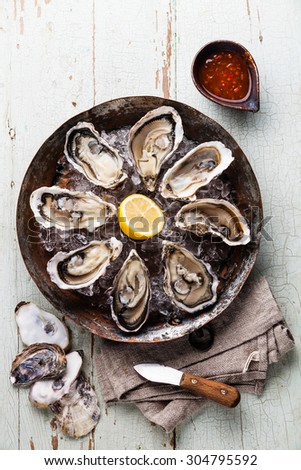Opened Oysters on metal copper plate on blue wooden background with spicy sauce and oyster knife