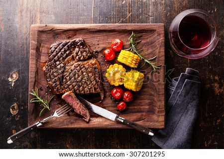 Sliced Medium rare grilled Steak Ribeye Black Angus with corn and cherry tomatoes on serving board block on wooden background