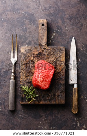 Raw fresh marbled meat Steak on meat cutting board and meat fork and kitchen knife on dark background