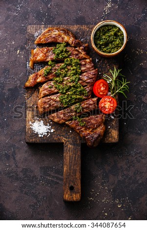 Sliced medium rare grilled beef barbecue Sirloin steak with chimichurri sauce on cutting board on dark background