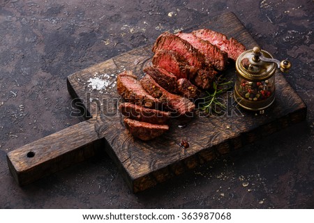Sliced medium rare grilled Beef steak and pepper mill on wooden cutting board