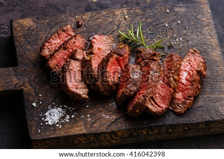 Sliced grilled steak roastbeef and rosemary on wooden cutting board background