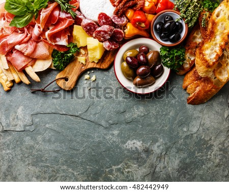 Italian food ingredients background with ham, salami, parmesan, olives, bread sticks on stone slate