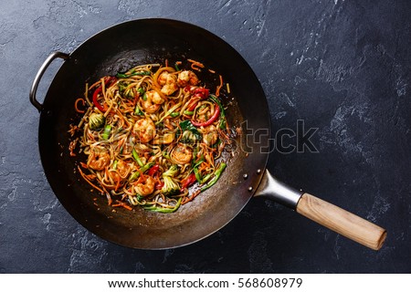 Udon stir-fry noodles with shrimp in wok pan on dark stone background