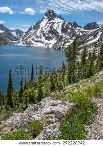 Sawtooth Lake in Idaho wilderness framed with pine trees and rugged snow capped mountain peaks.