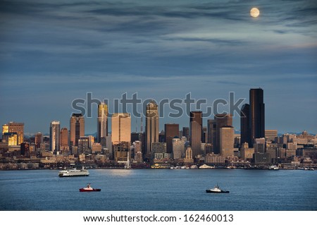 Moonrise Over Seattle, Washington. A full moon comes up over Elliott Bay and the Seattle Skyline. Tub boats and ferries work the waterfront area during this lovely sunset.