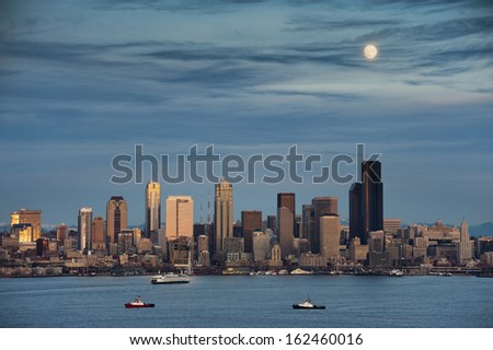 Moonrise Over Seattle, Washington. A full moon comes up over Elliott Bay and the Seattle Skyline. Tub boats and ferries work the waterfront area during this lovely sunset.