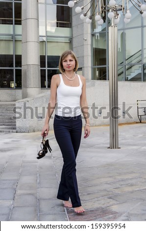 A young woman walks barefoot businessman after a hard day on the background of a modern business center