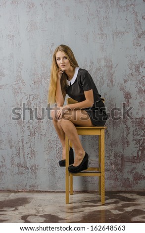 A young girl in a black dress and shoes poses with a high chair