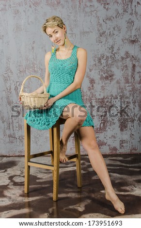 Cheerful girl with short hair in a short summer knit dress sitting on a chair with a basket