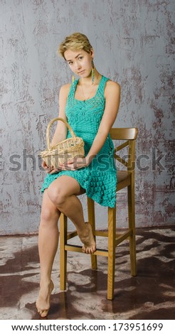 Cheerful girl with short hair in a short summer knit dress sitting on a chair with a basket