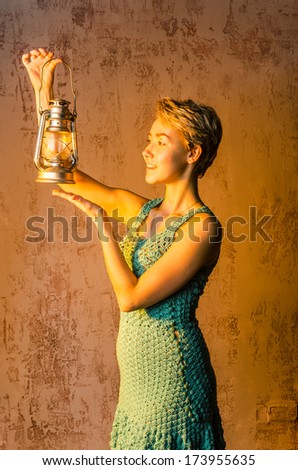 Cheerful girl with short hair in a short summer dress knit lit old kerosene lamp