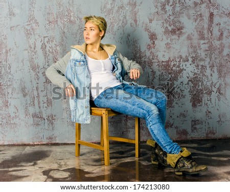 Young girl in jeans and jacket sitting on a chair and looking out for hamming coquettishly