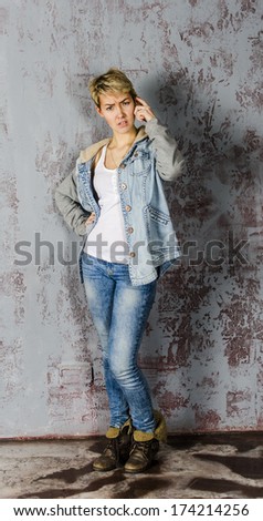 Young girl in jeans and a denim jacket standing near the wall