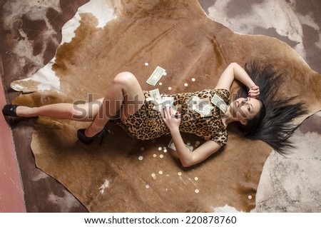 beautiful young brunette woman with long hair in a dress lies on a leopard skin backfilled money