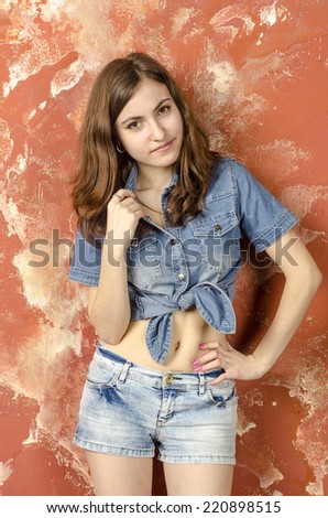 Young cheerful teenager girl in denim shorts and a shirt and long hair brown hair