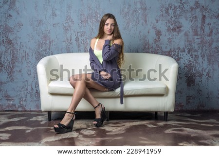 Beautiful young girl with long hair brown hair sitting on a sofa in a jacket and sandals