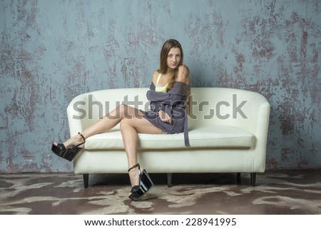 Beautiful young girl with long hair brown hair sitting on a sofa in a jacket and sandals