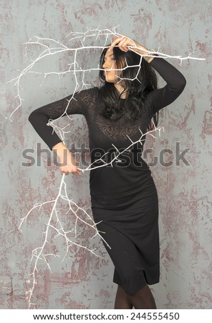 Young brunette girl in black dress dancing with sharp branches