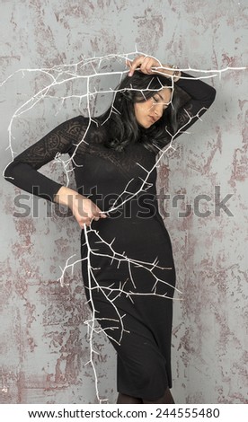 Young brunette girl in black dress dancing with sharp branches