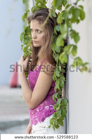 Beautiful long-haired girl in transparent top and is posing against a wall of ivy leaves