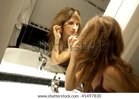 Beautiful Young Woman Making Up with Mascara in front of the Dresser