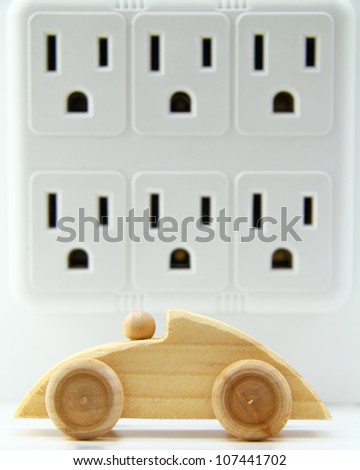 Wooden, toy car in front of a multi-electrical outlet adapter.