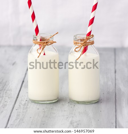 Two retro bottles of milk with striped straws standing on old table