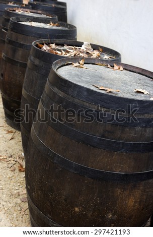 Wooden barrels standing by the wall covered by autumn leaves.