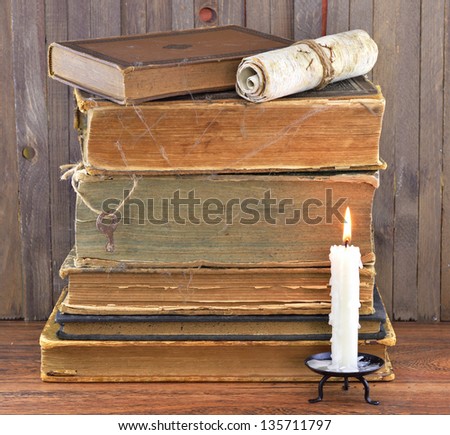 Old stacked books with candle and scroll in spider web
