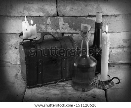 Black and white image of retro bottles with candles and wooden box in cellar background