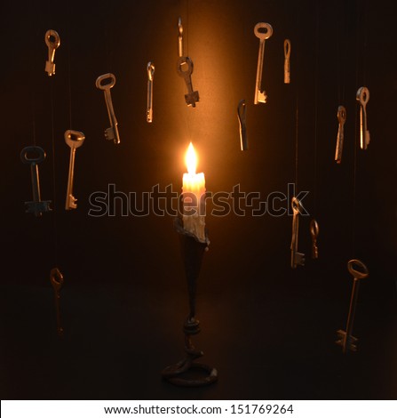 Single burning candle in candlestick with hanging metal keys
