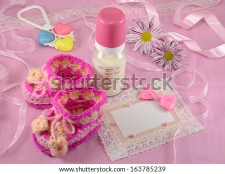 Pink greeting card with milk bottle and tiny booties for a girl on fabric background